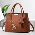 Detailed close-up of brown faux leather handbag with floral embroidery and butterfly charm - Earthy Yellow
