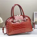 Detail of red crocodile embossed handbag with glossy finish and gold-tone hardware accents - Red