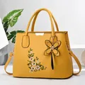 Close-up of yellow handbag featuring elegant floral embroidery and butterfly pendant - Yellow