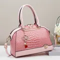 Detailansicht der rosa Handtasche mit Krokodilprägung, Goldbeschlägen und Kleeblatt - Rosa