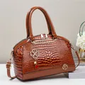 Close-up of brown crocodile embossed handbag with golden K logo and floral accessories - Earthy Yellow