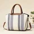 Close-up of contrast striped canvas bag featuring brown leather handles and metal hardware - White