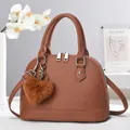 Close-up of brown litchi grain leather shell bag with a plush heart charm accessory - Earthy Yellow