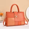 Close-up of the gold clasp with brand engraving and crocodile texture on the tote bag - Orange Red