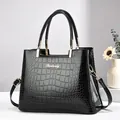 Elegante bolso de mano en charol negro con motivo de cocodrilo, logo dorado y asas - Negro