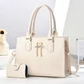 Close-up of beige lychee leather tote bag with swan metal buckle and pearl tassel detail - Off White