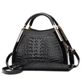 Detailed close-up of crocodile-embossed leather and gold hardware on black handbag - Black