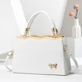 White Saffiano leather handbag with gold bow hardware and adjustable shoulder strap - White
