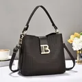 Detalle de bolso tipo cubo en cuero repujado negro con logo B dorado y asa superior - gris oscuro