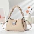 Detalle de bolso de cuero beige con asa plisada, cierre metálico y pies de protección - Blanco Roto
