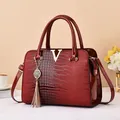 Sac à main rouge gaufré crocodile avec logo V doré et pompon dans un décor de vie élégant - Rouge