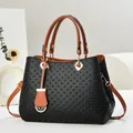 Detail of woven texture black shoulder bag with brown handles and gold hardware accents - Black