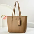 Close-up of brown litchi grain leather tote bag with logo plate and decorative charm - Khaki
