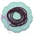 Cuentas de granato púrpura oscuro facetadas en un plato decorativo azul claro vintage - Granate