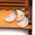 Three moon-shaped polished white crystal pendants with silver metal clasps on wood - White Crystal