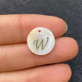 Golden letter W on white shell round charm pendant held by hand showing actual size - Letter W