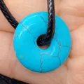 Turquoise pattern donut pendant necklace on black braided cord held in hand - Turquoise