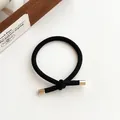 Elastic black knotted hair tie with gold metal end caps on white background - Black
