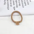 Detail of woven khaki hair scrunchie featuring a brown leather smiley face patch - Khaki