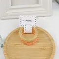 Details von gelben und orangefarbenen Spiralhaargummis auf Holztablett mit Packung - Orange