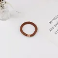 Détail d'un élastique tressé marron orné d'une perle dorée incrustée de strass brillants - Marron