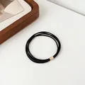 Black high-elastic multi-strand hair tie with gold metal clasp on white background - Black