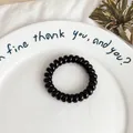 Elastic spiral hair tie in solid black color on a white decorative ceramic tray - Black