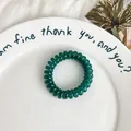 Dark green spiral phone cord hair tie on a white ceramic plate for ponytail styling - Teal