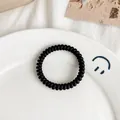 Elastic black spiral hair tie with matte finish on decorative ceramic plate - Matte Black