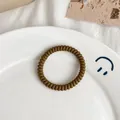 Elastic spiral hair tie in matte dark brown finish on a decorative ceramic plate - Matte Coffee