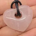 Natuurlijke rozenkwarts hart hanger met zwart koord vastgehouden in de hand - Rozenkwarts