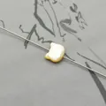 Macro view of a cat-shaped natural shell bead with iridescent luster on a display needle - Vertical Hole Cat Head / Yellow