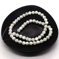 Macro shot of natural white shell beads with iridescent luster on a black matte tray - 2mm / White