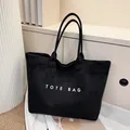 Chic black tote bag with white TOTE BAG lettering and spacious design for daily commute - Black