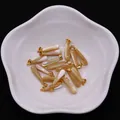 Makro-Detail von tropfenförmigen Muschel-Anhängern mit Goldösen in einer Porzellanschale - Braunes Muschel Gold