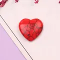 Detalle de una piedra turquesa roja en forma de corazón con vetas negras y flores - Howlita Roja