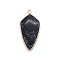 Détail d'un pendentif en pierre noire en forme de balle avec marbrures et bordure dorée - Howlite à Lignes Noires