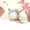 Close-up of a golden dragon claw pendant holding a white round natural stone bead - Opal