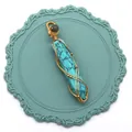 Vue détaillée d'un pendentif hexagonal en turquoise enroulé de fil doré sur un support bleu - Turquoise Bleue
