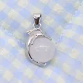 Detailed view of a silver dolphin pendant clutching a smooth white round gemstone bead - 14x23mm / White Crystal