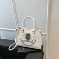 White faux leather tote bag with metallic skull and studs on vintage book background - White