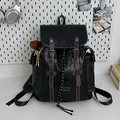 Retro black leather backpack featuring brown straps and fuzzy ball accessory on a desk - With Charm / Black