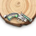 Macro detail of gun-shaped pendant with abalone shell inlay on natural wood background - Pistol Shape / 36x57mm