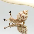 Vista macro lateral del broche de caracol dorado con patrón de concha y ojos negros - 24x49mm / Estilo Babylonia Dorado (B250606055)