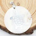 Pendentif rond en nacre blanche avec tortue argentée incrustée sur fond en bois naturel - Style Tortue de Mer Ronde