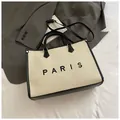 Beige geweven draagtas met zwarte PARIS belettering en zwarte schouderbanden - Groot Beige en Zwart