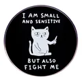 Round black enamel pin featuring a small white cartoon cat holding a knife with humor text - Black Cat Fight Me