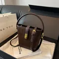 Bolso cubo de gamuza marrón oscuro con cierre dorado y elegante asa superior - café