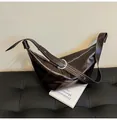 Detail of dark brown glossy croissant bag on leather bench with modern metal buckle - Coffee