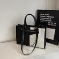 Elegante bolso de lona bicolor en blanco y negro con asas de cuero y correa larga. - Negro